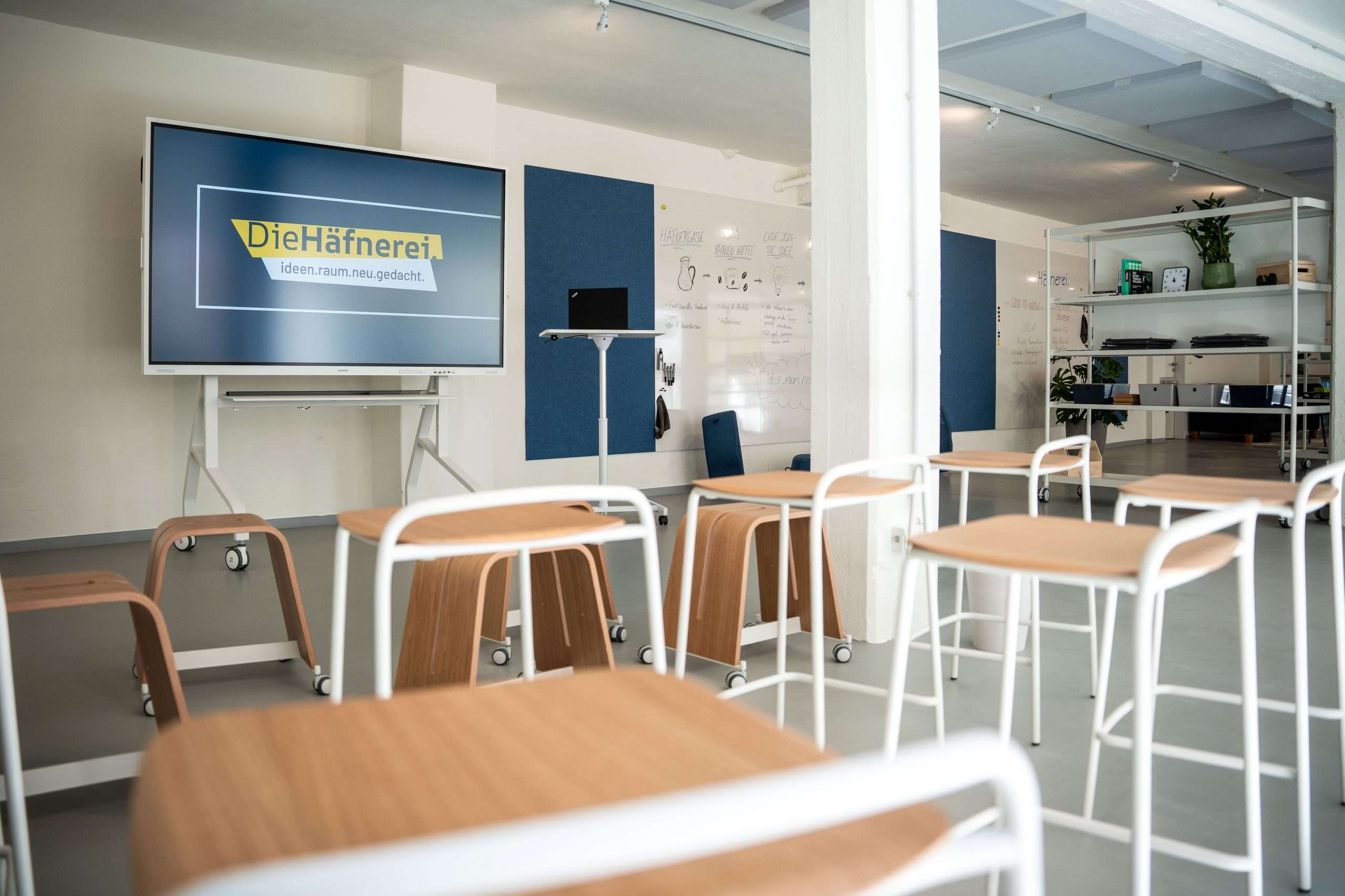 Moderner Seminar- und Workshopraum der Die Häfnerei in Würzburg mit Präsentationsdisplay, Whiteboard, Stehtisch und flexibel angeordneten Tischen und Stühlen.
