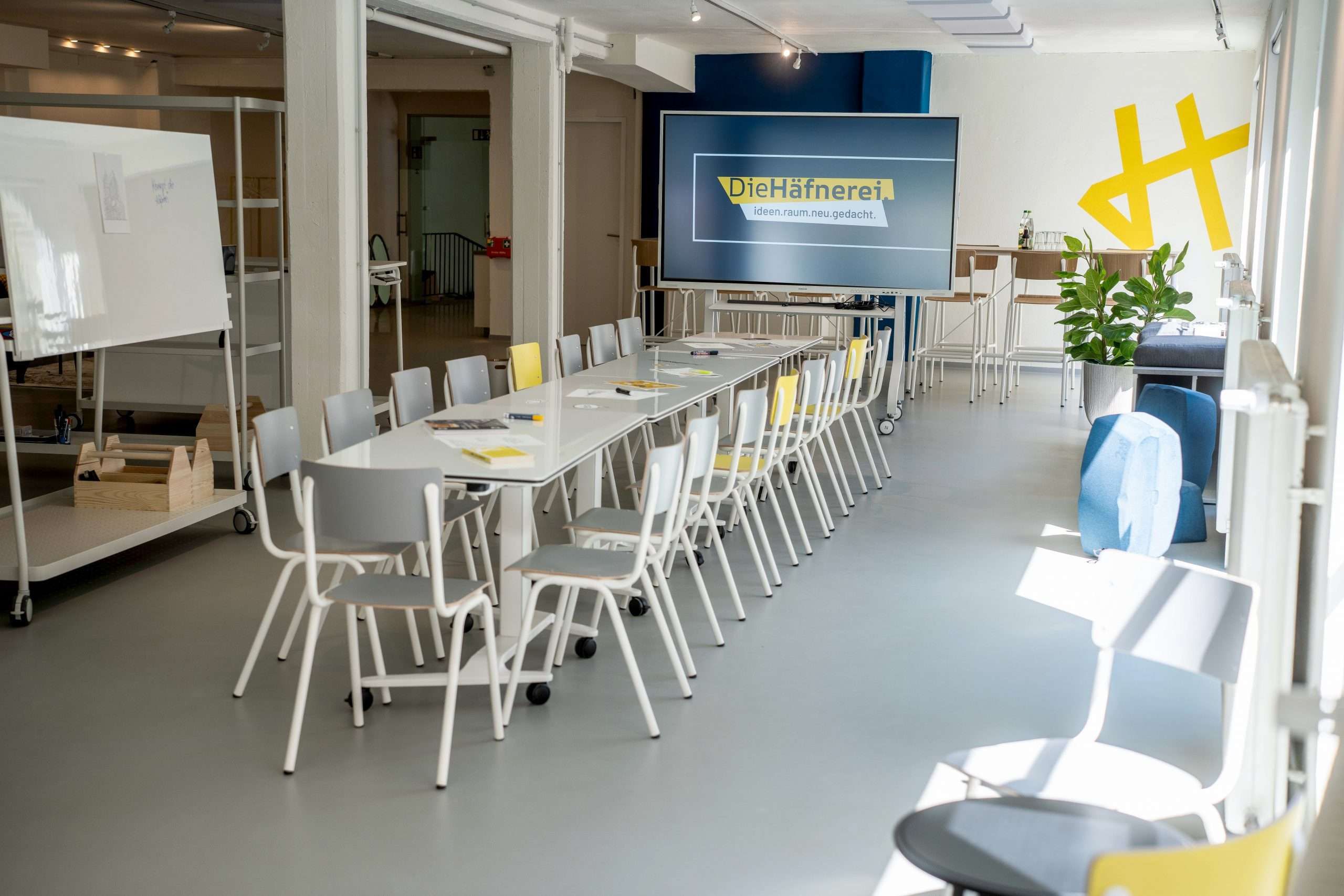 Moderner Workshop- und Meetingraum der Häfnerei in Würzburg mit Konferenztischen, Stühlen, Whiteboard und großem Präsentationsdisplay.