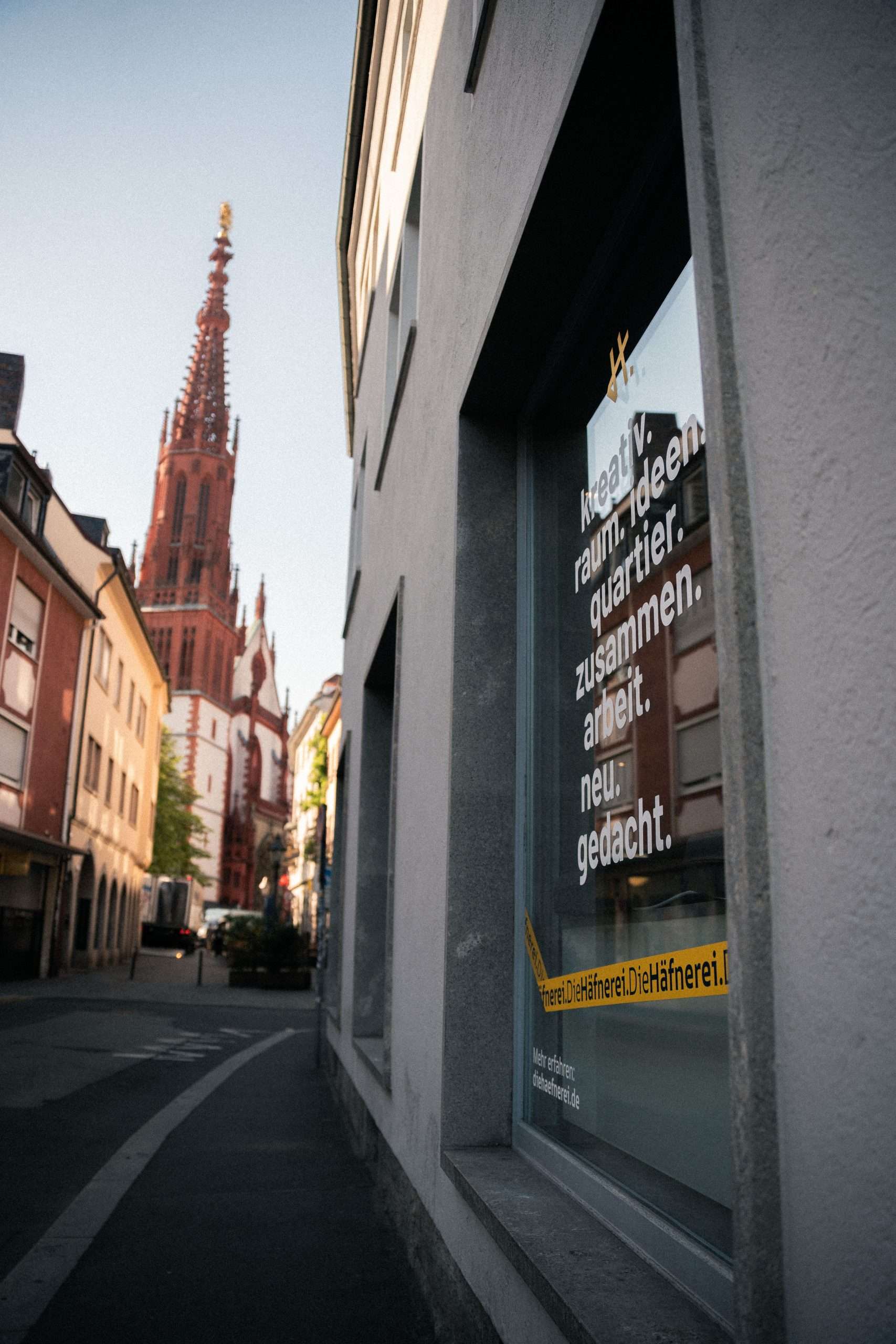 Außenansicht der Häfnerei in der Würzburger Altstadt mit beschriftetem Schaufenster und Blick auf die Marienkapelle im Hintergrund.