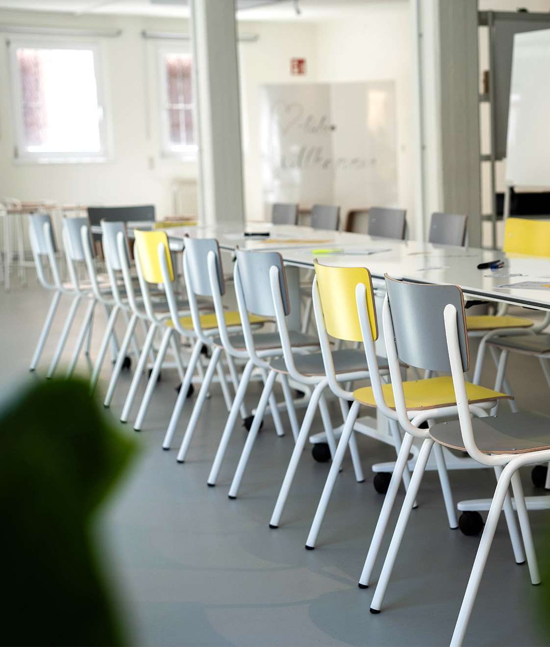 Heller Workshop- und Seminarraum Die Häfnerei in Würzburg mit flexibel angeordneten Tischen und grauen sowie gelben Stühlen.