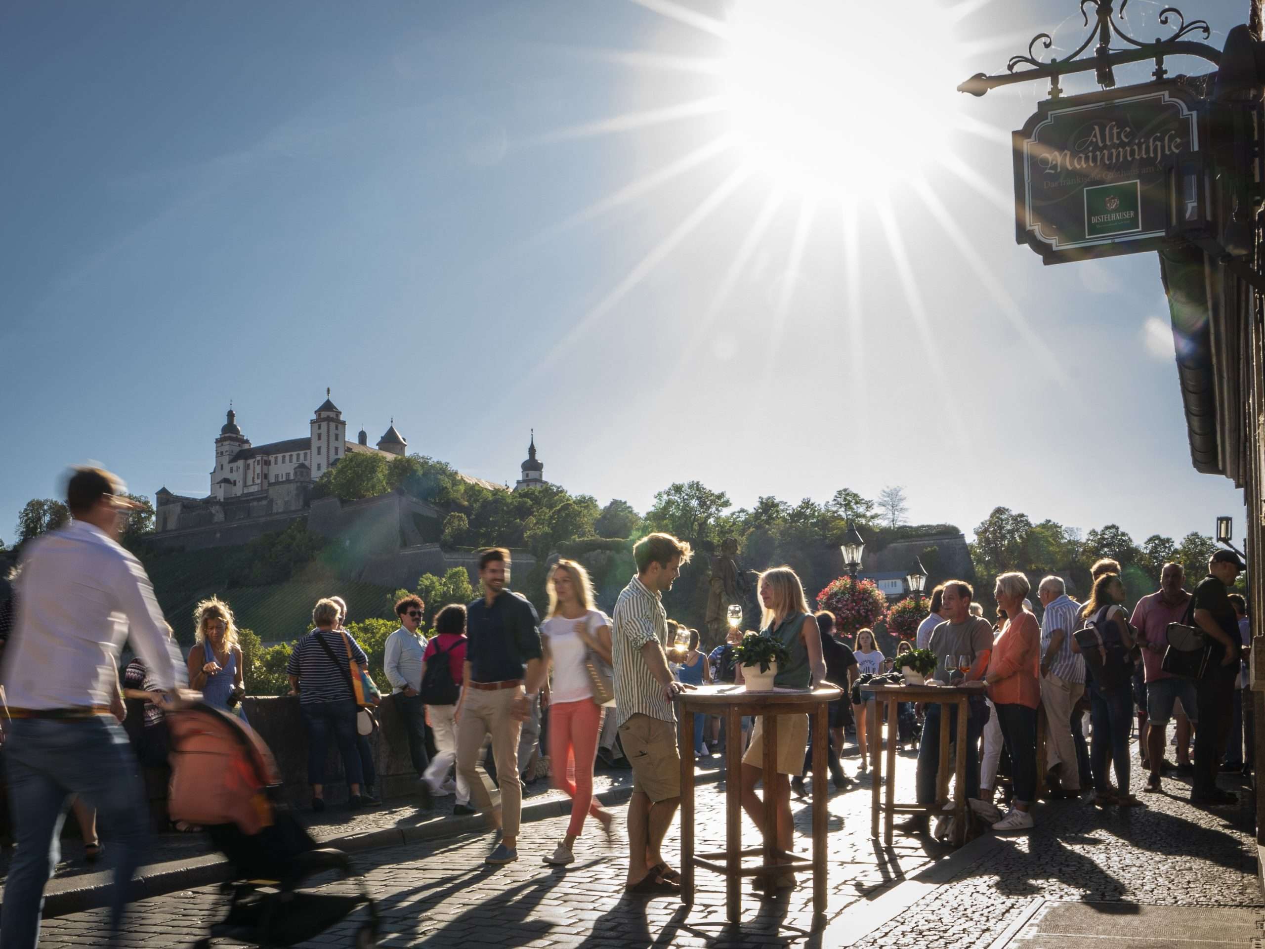 Besucher genießen Wein beim Brückenschoppen in Würzburg mit Blick auf die Festung Marienberg